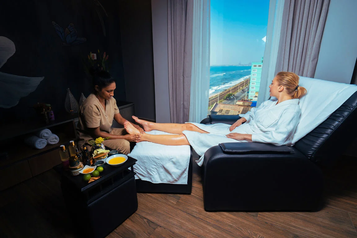 A serene spa session in progress with a therapist providing a foot massage to a relaxed client in a tranquil room with a picturesque ocean view through large windows.